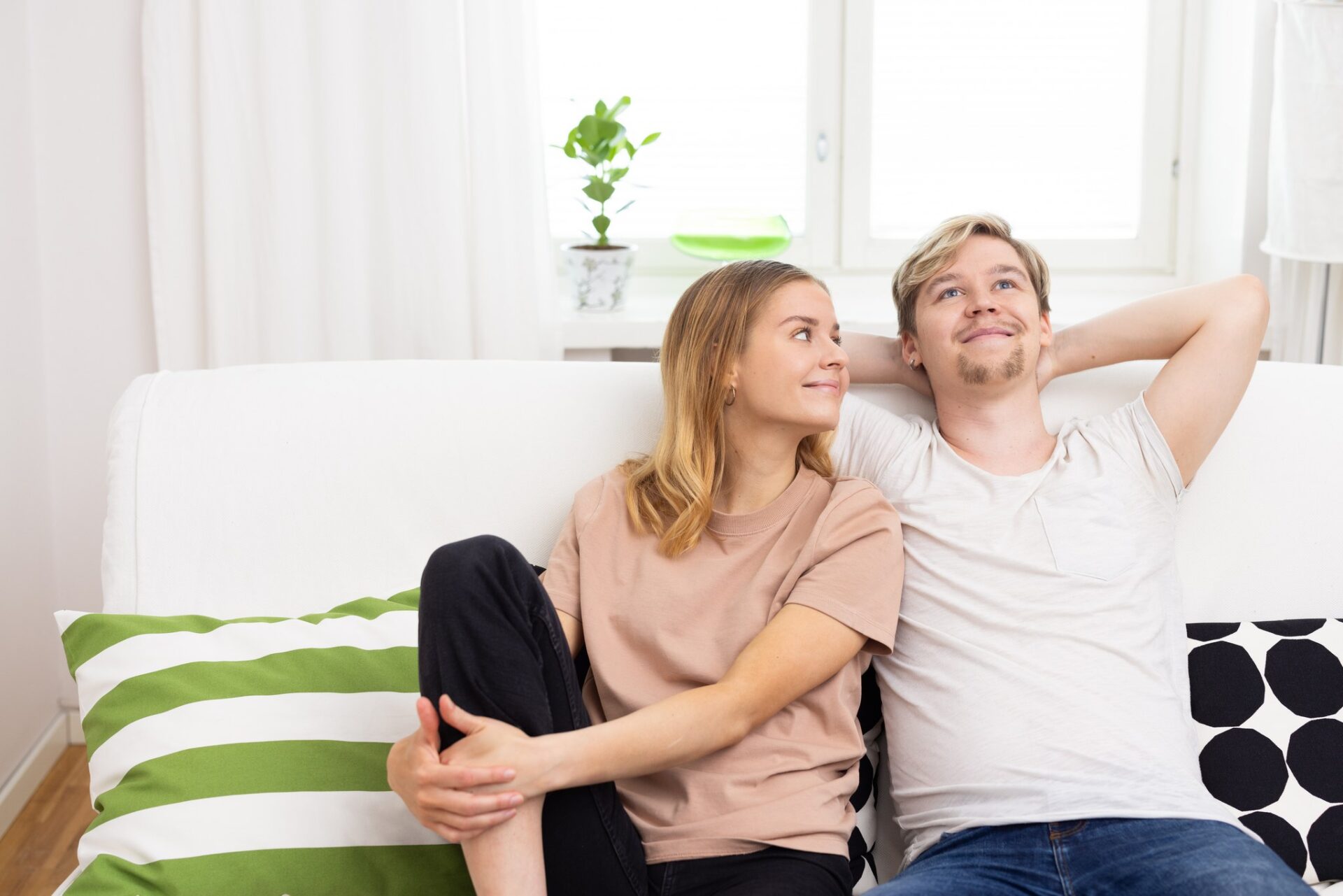 mies ja nainen istuu sohvalla, miehellä kädet ristittynä pääntaakse, nainen miheen kainalossa